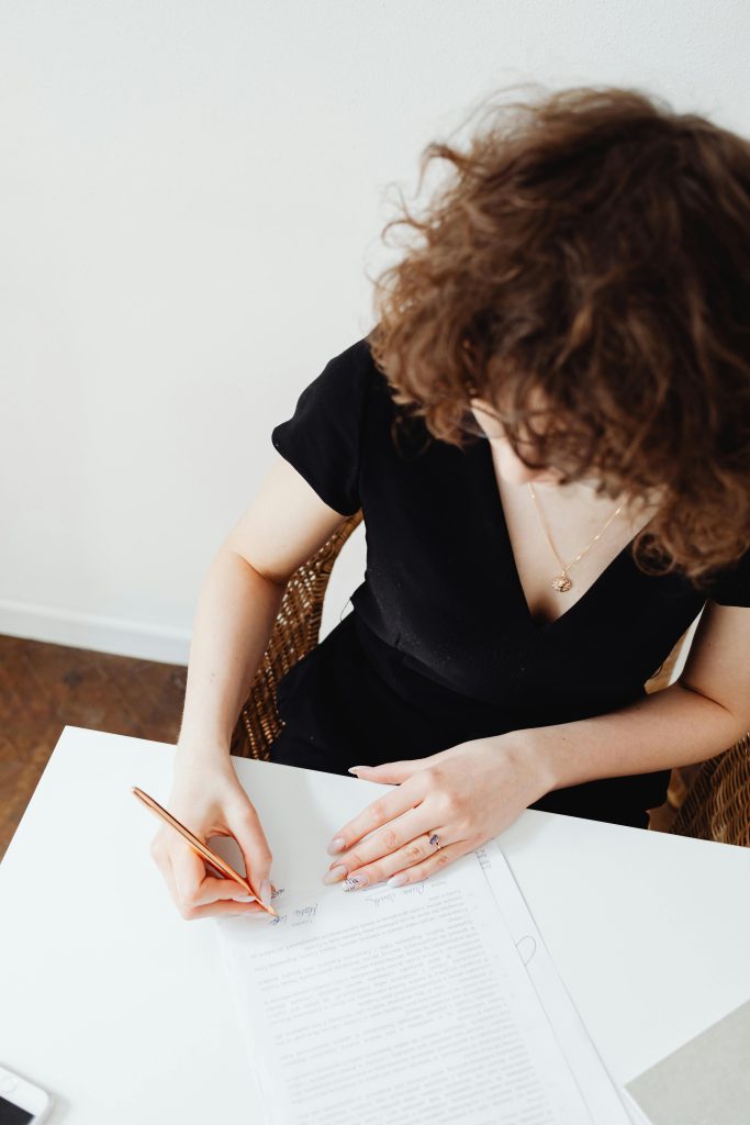 pexels-photo-7681245-7681245 A woman with curly hair signing official documents at a workplace.